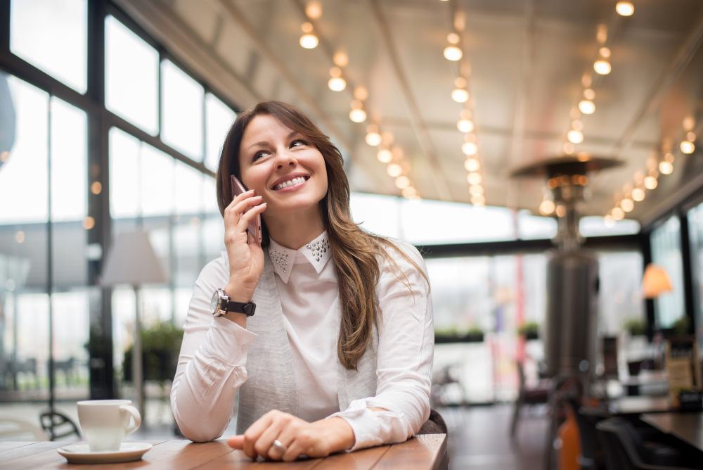 Charming woman calling with cell telephone while sitting in coffee shop | Proven Tips To Making A Sales Voicemail Script | sales prospecting